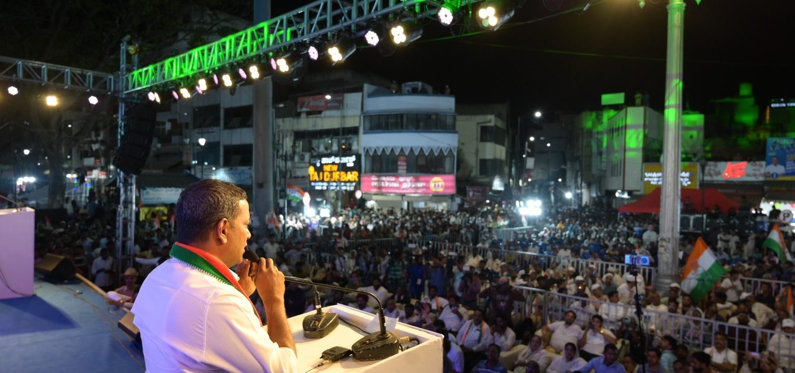 Mansoor Ali Khan addressing a large public rally at night.